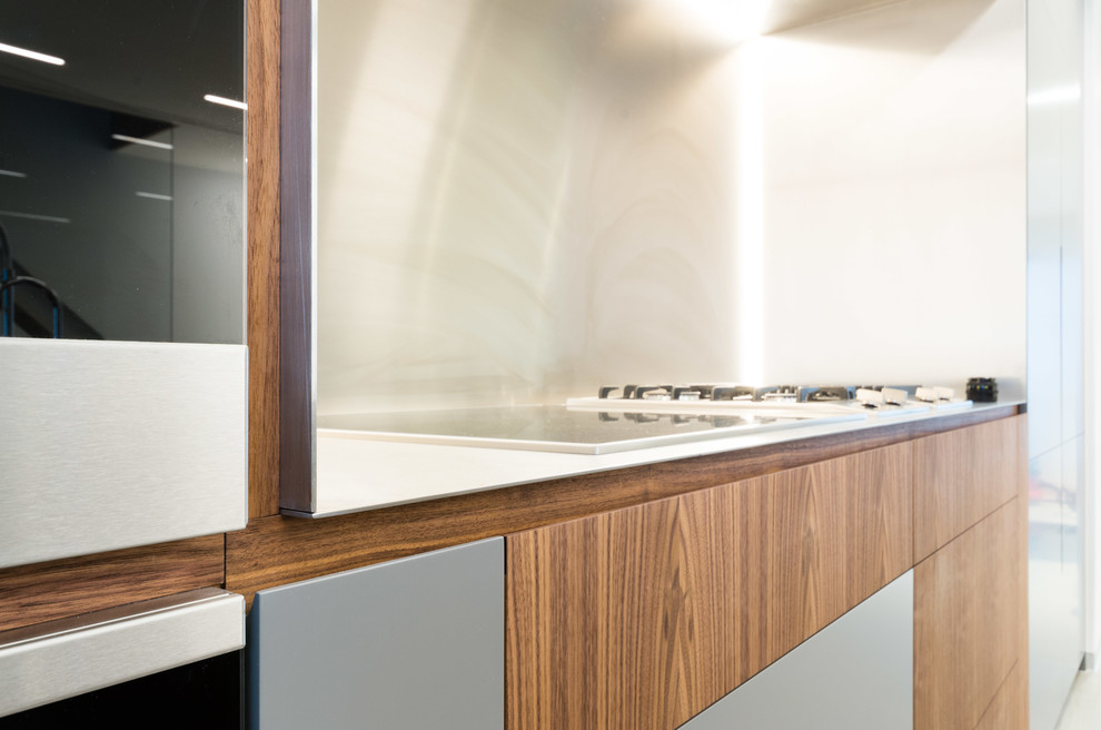 Design ideas for a medium sized contemporary l-shaped open plan kitchen in London with a submerged sink, flat-panel cabinets, dark wood cabinets, metallic splashback, metal splashback, black appliances, porcelain flooring, an island, beige floors, grey worktops and granite worktops.