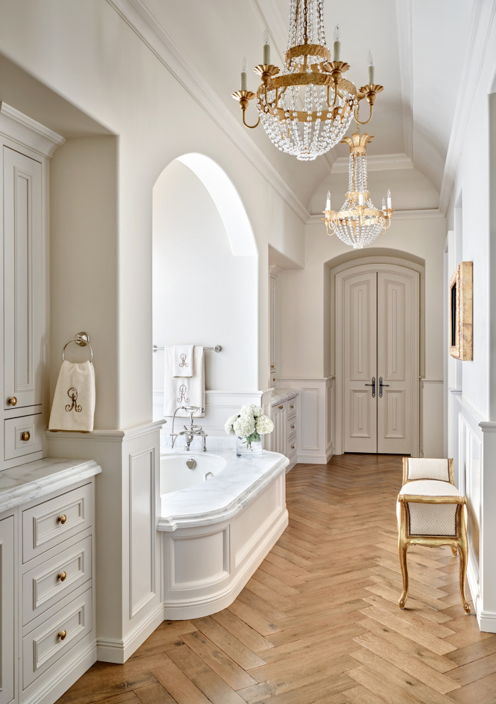 Design ideas for a mediterranean bathroom in Phoenix with recessed-panel cabinets, grey cabinets, an undermount tub, white walls, medium hardwood floors, brown floor, white benchtops, a built-in vanity, recessed and decorative wall panelling.
