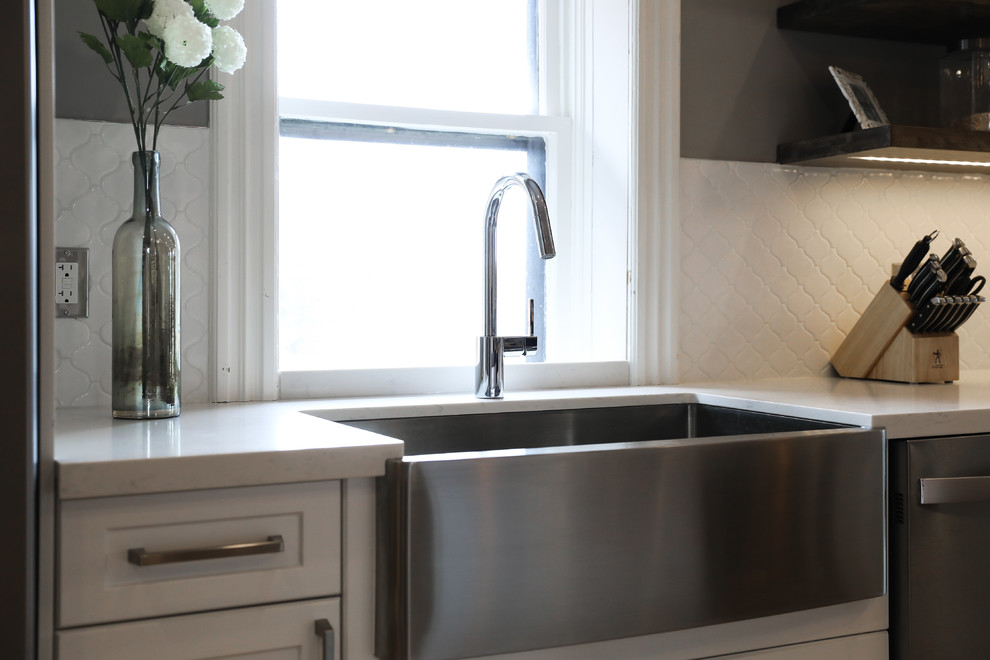 Inspiration for a mid-sized transitional single-wall medium tone wood floor and brown floor eat-in kitchen remodel with a farmhouse sink, shaker cabinets, white cabinets, white backsplash, stainless steel appliances, an island and white countertops