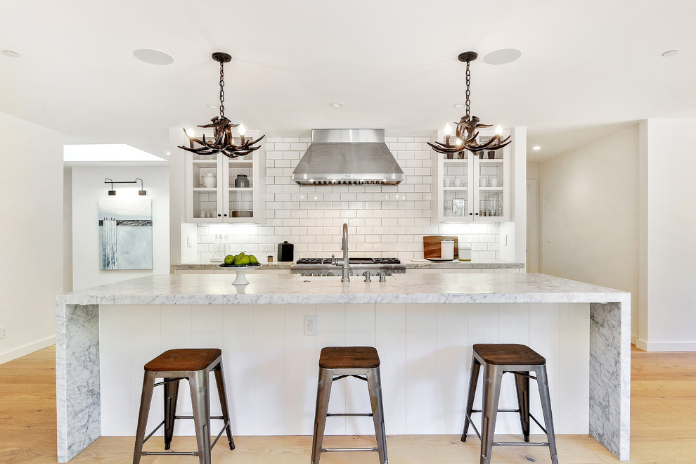 Transitional galley kitchen in San Francisco with a farmhouse sink, glass-front cabinets, white splashback, subway tile splashback, stainless steel appliances, medium hardwood floors and with island.