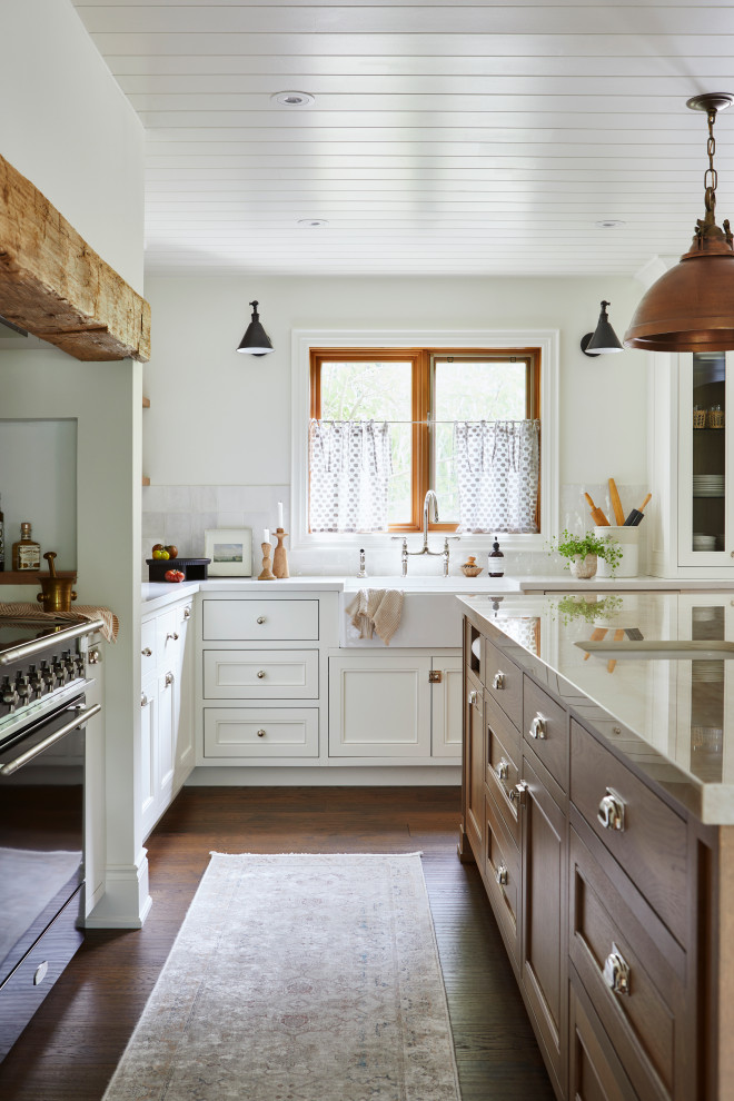 Large beach style l-shaped open plan kitchen with a farmhouse sink, shaker cabinets, light wood cabinets, solid surface benchtops, white splashback, ceramic splashback, panelled appliances, medium hardwood floors, with island, brown floor, beige benchtop and timber.