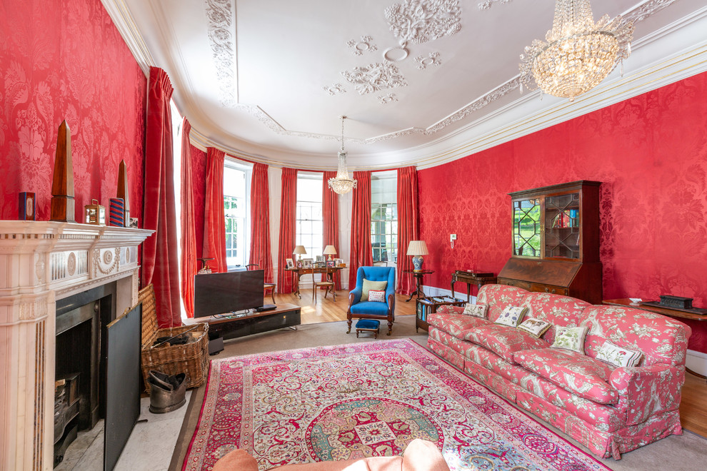 This is an example of a traditional living room with red walls, medium hardwood flooring, a standard fireplace and brown floors.