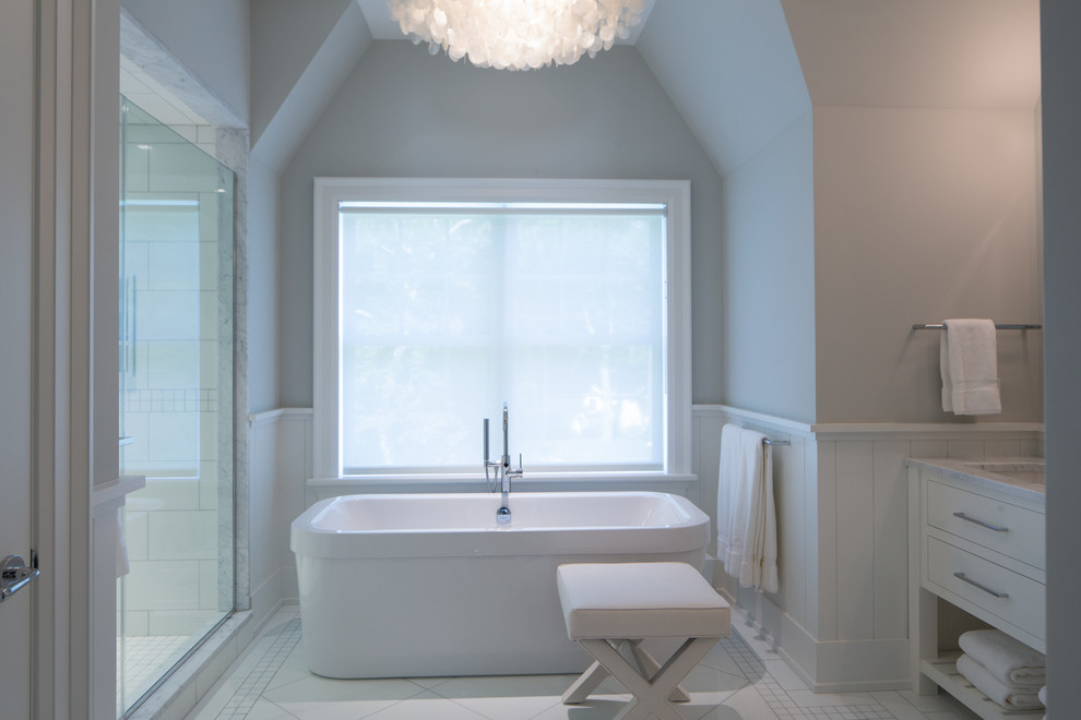 Photo of a transitional master bathroom in New York with an undermount sink, furniture-like cabinets, white cabinets, marble benchtops, a freestanding tub, a double shower, a one-piece toilet, white tile, glass tile and white walls.
