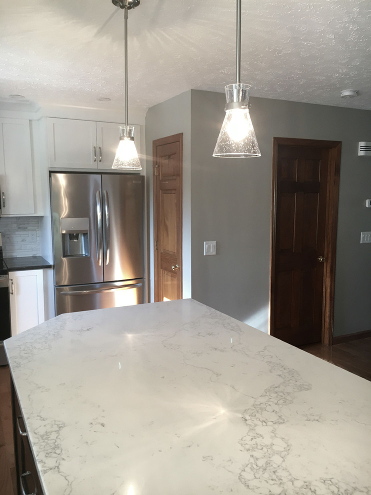 Example of a large transitional single-wall medium tone wood floor eat-in kitchen design with an undermount sink, shaker cabinets, white cabinets, granite countertops, multicolored backsplash, marble backsplash, stainless steel appliances, an island and black countertops