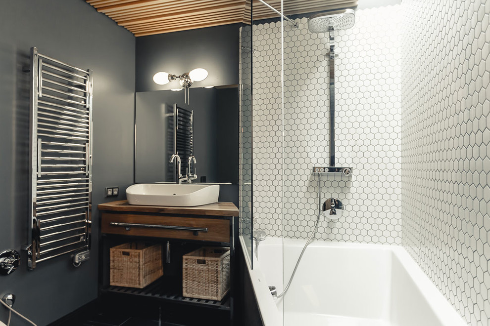 This is an example of a mid-sized industrial master bathroom in Moscow with flat-panel cabinets, light wood cabinets, an alcove tub, a shower/bathtub combo, a wall-mount toilet, white tile, porcelain tile, grey walls, slate floors, a drop-in sink, wood benchtops, black floor, a shower curtain and beige benchtops.