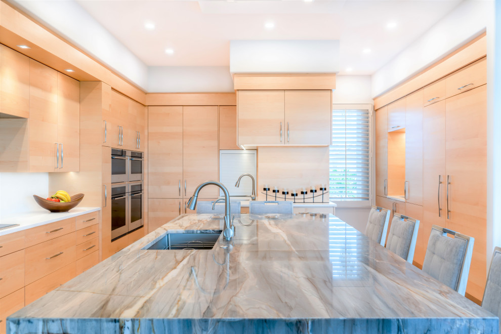 Large trendy u-shaped light wood floor and beige floor eat-in kitchen photo with an undermount sink, flat-panel cabinets, light wood cabinets, white backsplash, paneled appliances, an island and gray countertops