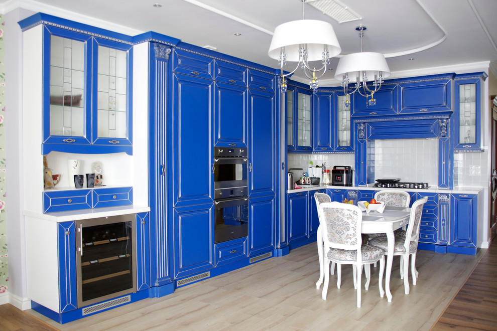 Inspiration for a large traditional l-shaped eat-in kitchen in Moscow with blue cabinets, marble benchtops, white splashback, ceramic splashback, stainless steel appliances, light hardwood floors, raised-panel cabinets and no island.