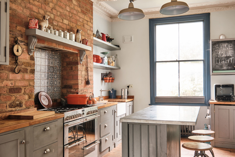 This is an example of a large eclectic galley open plan kitchen in London with a belfast sink, shaker cabinets, grey cabinets, zinc worktops, blue splashback, ceramic splashback, coloured appliances, medium hardwood flooring, an island, grey worktops and a chimney breast.