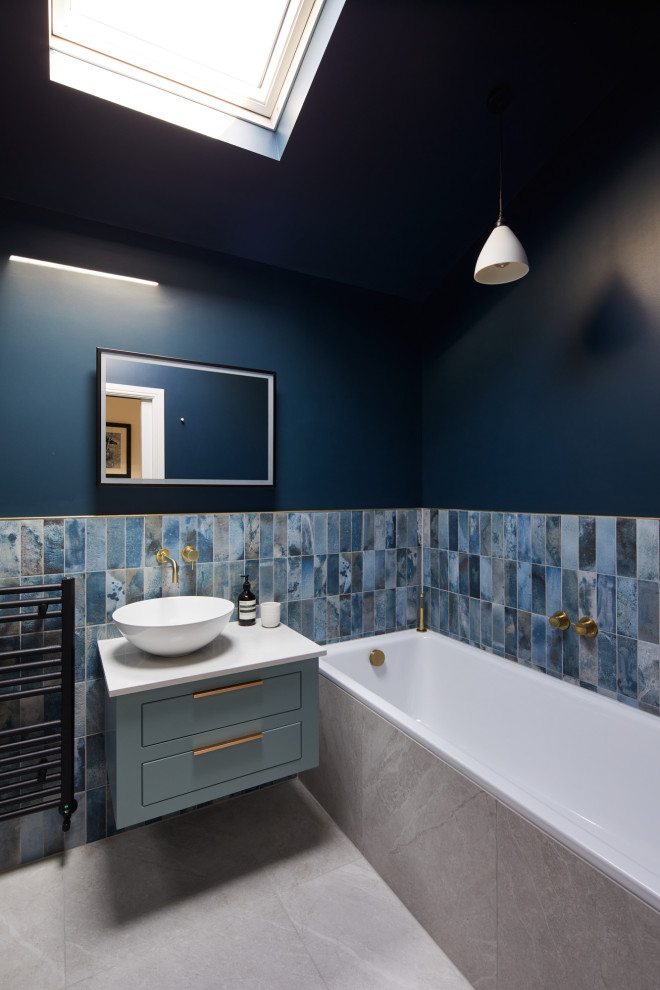Aménagement d'une salle de bain grise et jaune contemporaine de taille moyenne pour enfant avec un placard à porte plane, des portes de placard bleues, une baignoire posée, une douche ouverte, WC suspendus, un carrelage bleu, des carreaux de porcelaine, un mur bleu, un sol en carrelage de porcelaine, une vasque, un plan de toilette en surface solide, un sol gris, une cabine de douche à porte battante, un plan de toilette gris, meuble simple vasque et meuble-lavabo suspendu.