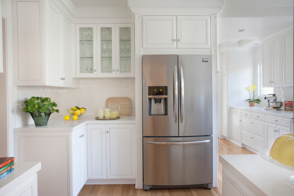 Enclosed kitchen - mid-sized transitional l-shaped light wood floor enclosed kitchen idea in Los Angeles with a drop-in sink, beaded inset cabinets, white cabinets, quartzite countertops, white backsplash, subway tile backsplash, stainless steel appliances and an island