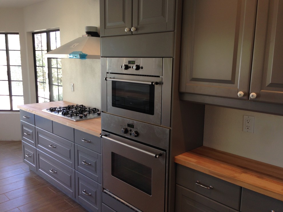 Transitional u-shaped laminate floor and brown floor enclosed kitchen photo with shaker cabinets, blue cabinets, wood countertops and stainless steel appliances