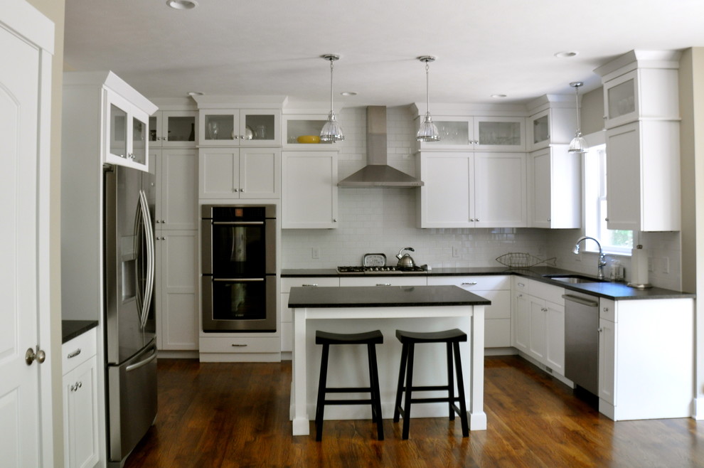 This is an example of a transitional l-shaped open plan kitchen in Grand Rapids with a double-bowl sink, shaker cabinets, yellow cabinets, granite benchtops, white splashback, porcelain splashback, stainless steel appliances, medium hardwood floors and with island.