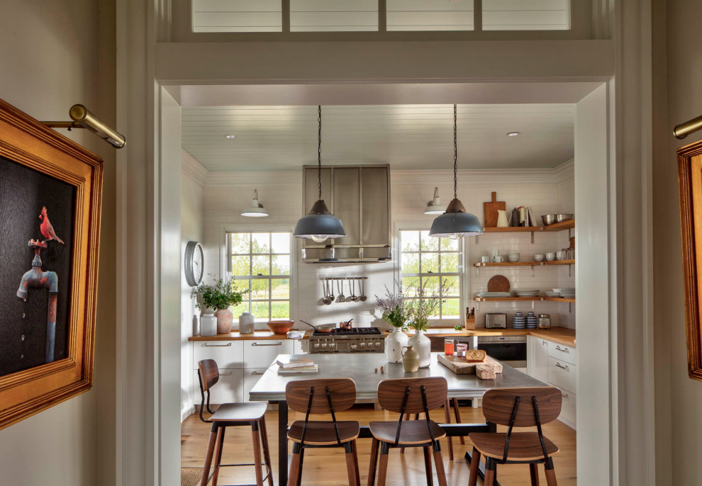 Design ideas for a mid-sized country l-shaped eat-in kitchen in Baltimore with flat-panel cabinets, white cabinets, wood benchtops, white splashback, subway tile splashback, stainless steel appliances, light hardwood floors, with island, brown floor, brown benchtop and timber.