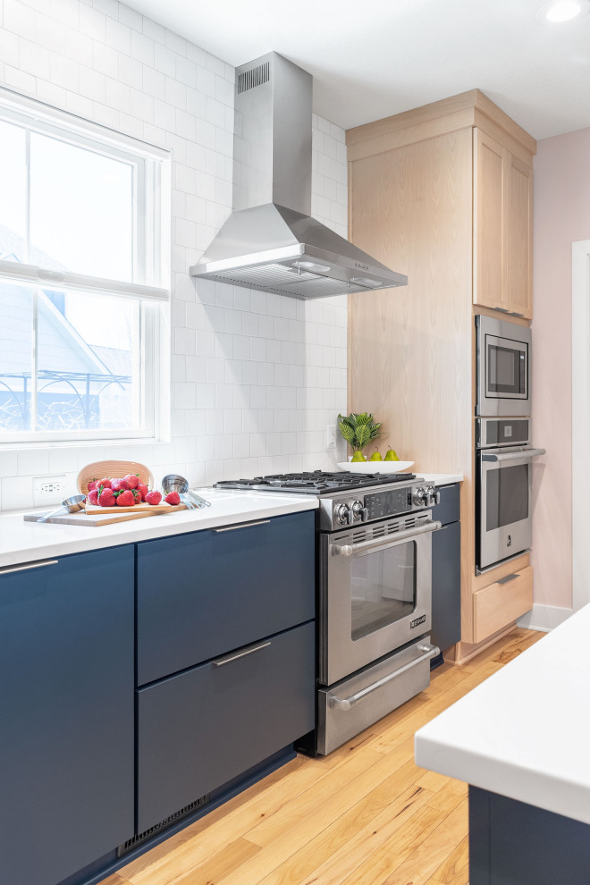 Inspiration for a mid-sized modern l-shaped eat-in kitchen in Minneapolis with flat-panel cabinets, blue cabinets, quartz benchtops, white splashback, subway tile splashback, stainless steel appliances, vinyl floors, brown floor and white benchtop.