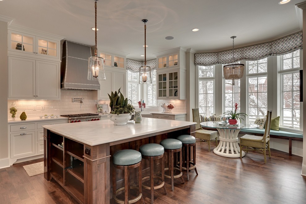 This is an example of a traditional l-shaped eat-in kitchen in Minneapolis with shaker cabinets, white cabinets, white splashback, subway tile splashback and stainless steel appliances.