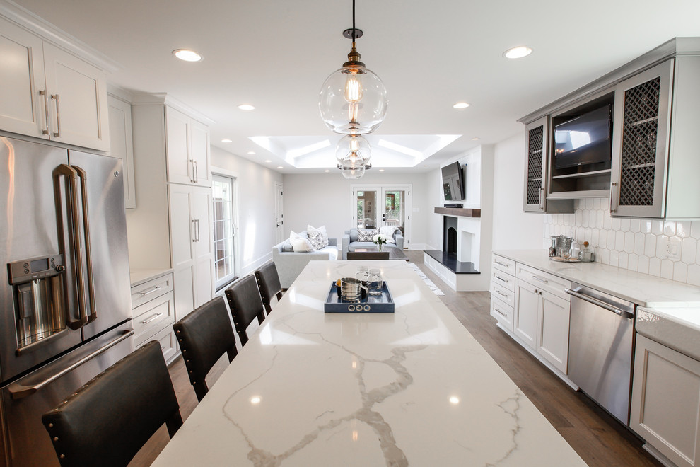 Large transitional l-shaped medium tone wood floor open concept kitchen photo in Chicago with a farmhouse sink, recessed-panel cabinets, white cabinets, marble countertops, white backsplash, porcelain backsplash, stainless steel appliances and an island