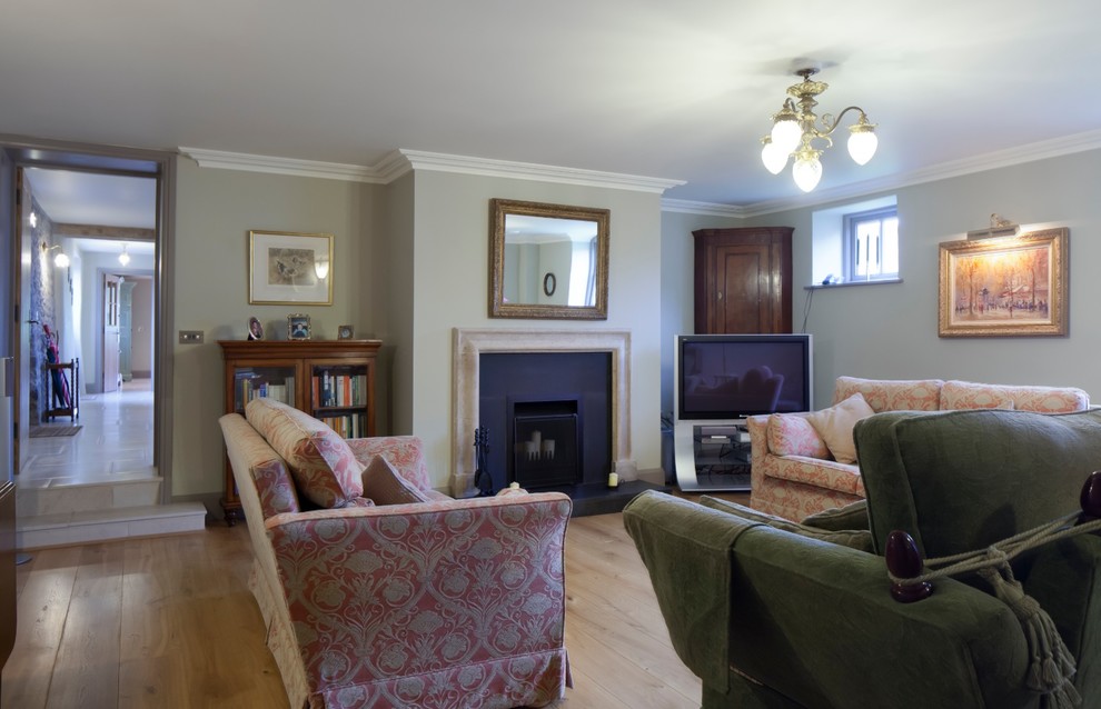 Transitional enclosed living room in Gloucestershire with medium hardwood floors, a standard fireplace, a stone fireplace surround and a freestanding tv.