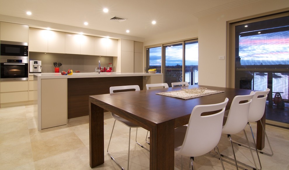 This is an example of a mid-sized contemporary galley open plan kitchen in Sydney with an undermount sink, flat-panel cabinets, beige cabinets, quartz benchtops, brown splashback, glass sheet splashback, stainless steel appliances, travertine floors, with island, beige floor and beige benchtop.