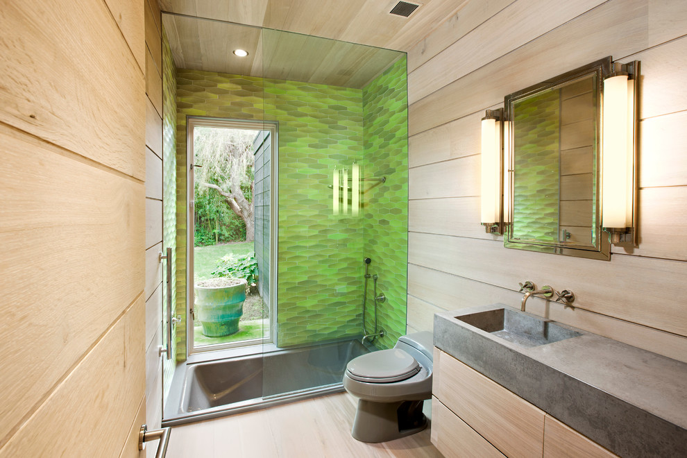 Mid-sized contemporary bathroom in New York with an integrated sink, flat-panel cabinets, light wood cabinets, concrete benchtops, a drop-in tub, a shower/bathtub combo, a one-piece toilet, green tile, beige walls, light hardwood floors and grey benchtops.