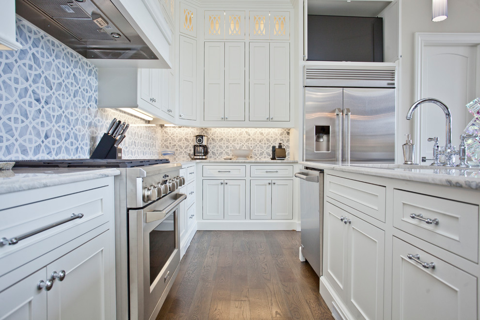 This is an example of a large mediterranean u-shaped eat-in kitchen in Other with an undermount sink, recessed-panel cabinets, white cabinets, granite benchtops, blue splashback, ceramic splashback, stainless steel appliances, medium hardwood floors, with island, brown floor and white benchtop.