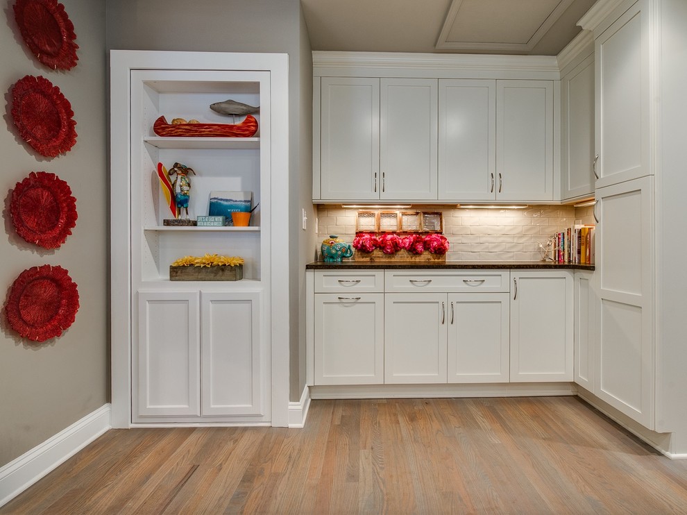 This is an example of a mid-sized contemporary l-shaped open plan kitchen in Charlotte with an undermount sink, recessed-panel cabinets, white cabinets, granite benchtops, beige splashback, stainless steel appliances, light hardwood floors, with island and beige floor.