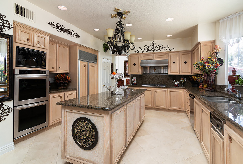 Photo of a mediterranean l-shaped separate kitchen in Los Angeles with a double-bowl sink, recessed-panel cabinets, light wood cabinets, brown splashback, with island, beige floor, brown benchtop, granite benchtops, panelled appliances and travertine floors.