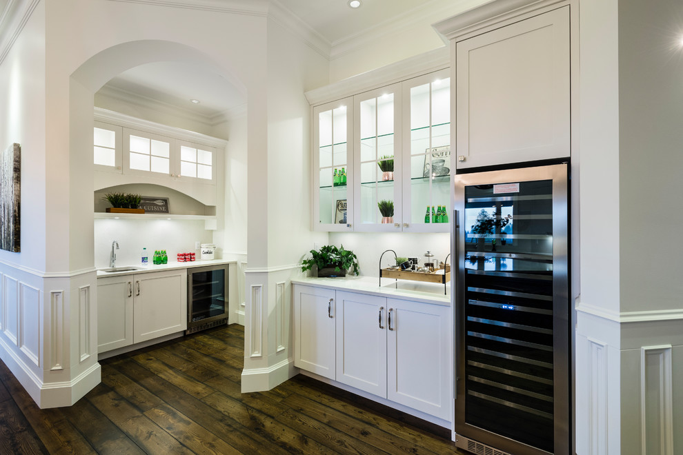 Huge mountain style u-shaped medium tone wood floor and brown floor open concept kitchen photo in Vancouver with an undermount sink, shaker cabinets, white cabinets, solid surface countertops, white backsplash, stone slab backsplash, stainless steel appliances, an island and white countertops