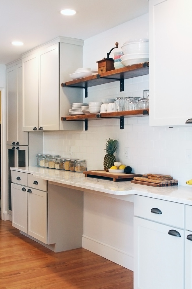 Mid-sized transitional galley medium tone wood floor kitchen pantry photo in Boston with a farmhouse sink, recessed-panel cabinets, white cabinets, marble countertops, white backsplash, subway tile backsplash, stainless steel appliances, an island and white countertops