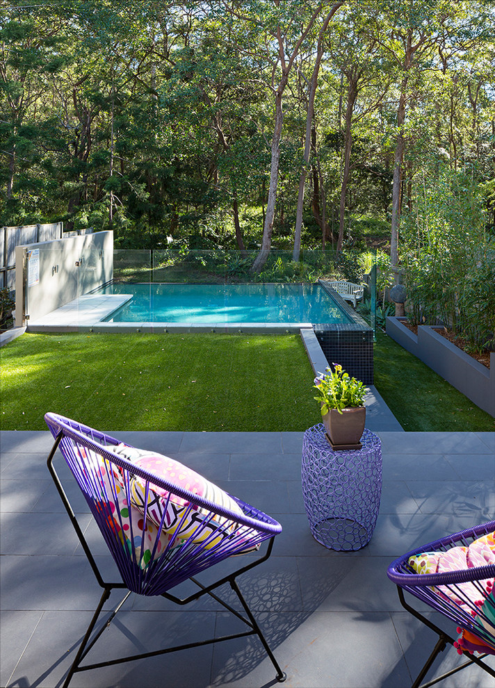 Contemporary backyard rectangular infinity pool in Brisbane with tile.