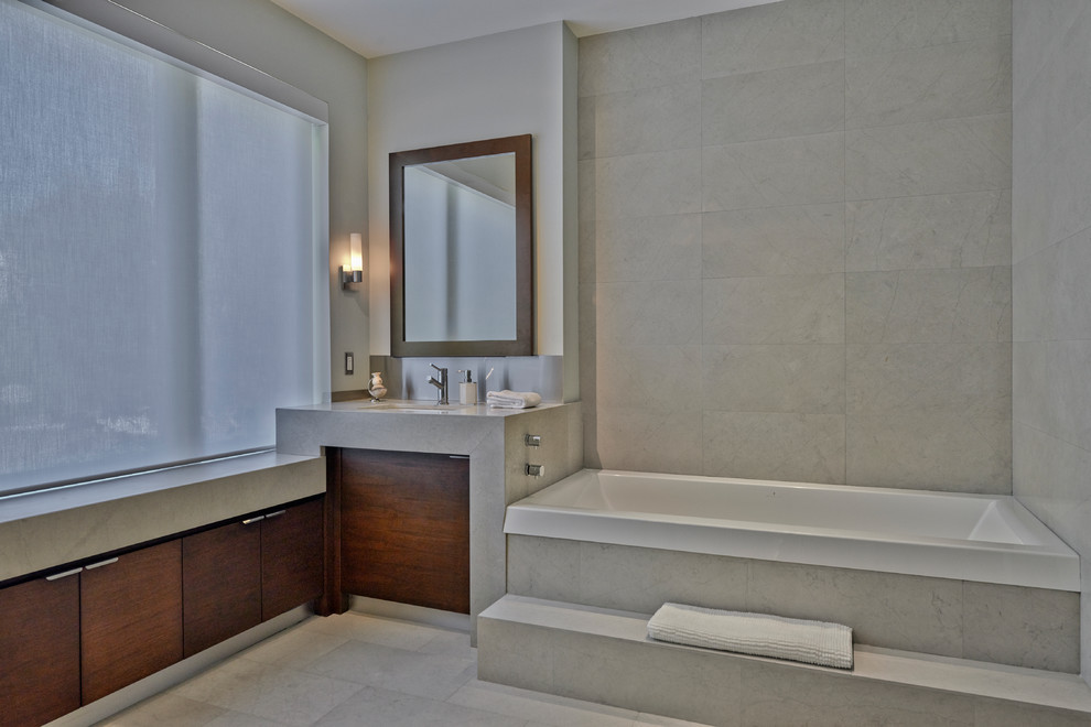 Photo of a mid-sized contemporary master bathroom in Toronto with an integrated sink, flat-panel cabinets, dark wood cabinets, a drop-in tub, gray tile and grey walls.