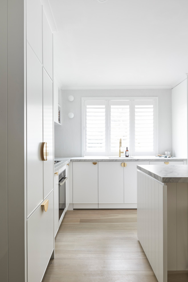 This is an example of a mid-sized modern l-shaped open plan kitchen in Sydney with an undermount sink, flat-panel cabinets, white cabinets, quartz benchtops, white splashback, light hardwood floors and white benchtop.