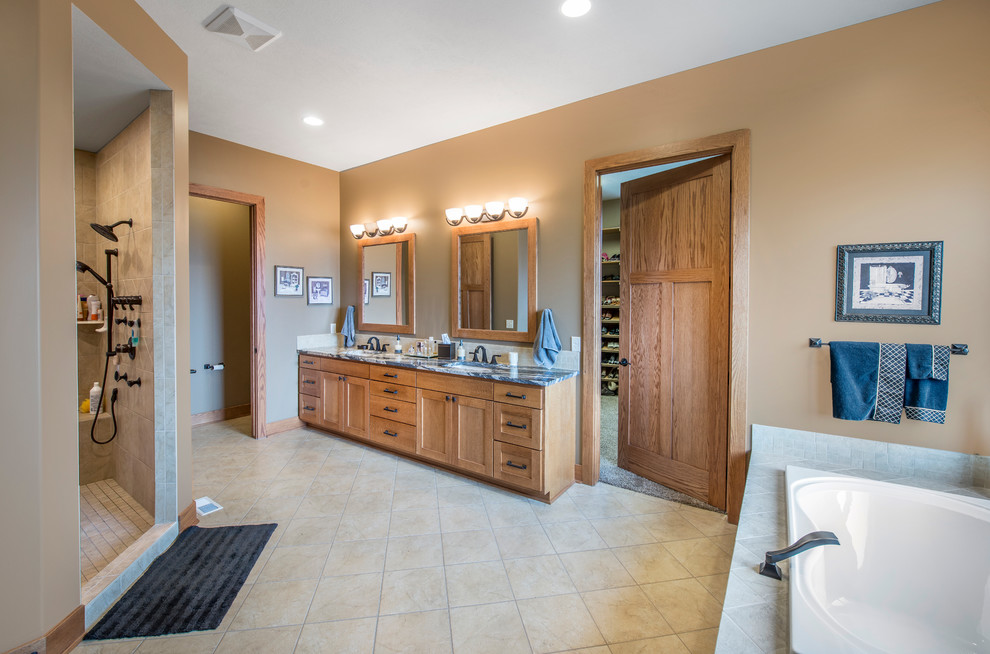 This is an example of an arts and crafts master bathroom in Omaha with an undermount sink, light wood cabinets, laminate benchtops, a drop-in tub, beige tile, porcelain floors and beige walls.