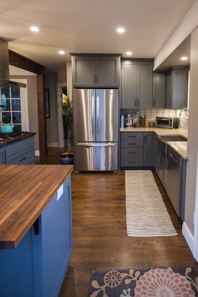 Example of a small transitional l-shaped dark wood floor and brown floor open concept kitchen design in Seattle with a farmhouse sink, shaker cabinets, gray cabinets, stainless steel appliances, an island, granite countertops, white backsplash, porcelain backsplash and beige countertops