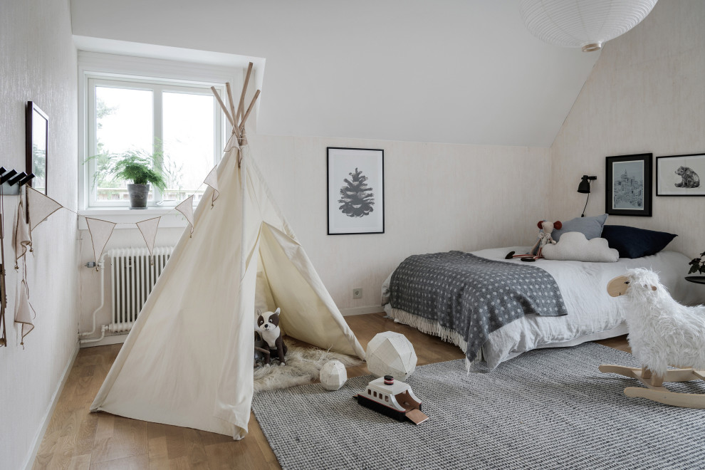 This is an example of a scandinavian gender-neutral kids' bedroom in Gothenburg with beige walls, medium hardwood floors and brown floor.