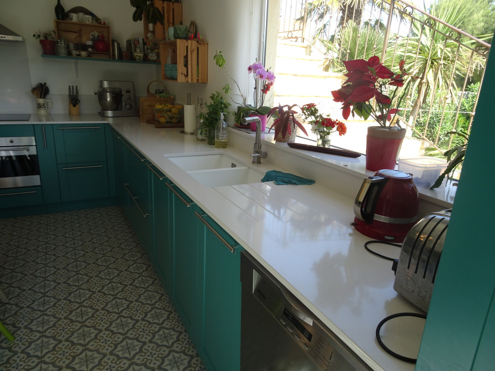 Klassisk inredning av ett stort vit vitt l-kök, med en undermonterad diskho, luckor med infälld panel, turkosa skåp, bänkskiva i kvartsit, vitt stänkskydd, rostfria vitvaror, cementgolv och blått golv