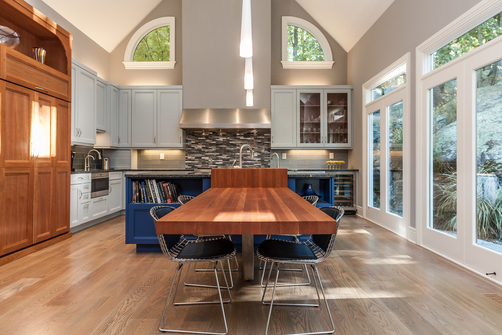 Large scandinavian l-shaped open plan kitchen in Raleigh with an undermount sink, recessed-panel cabinets, blue cabinets, wood benchtops, grey splashback, glass tile splashback, stainless steel appliances, medium hardwood floors and with island.