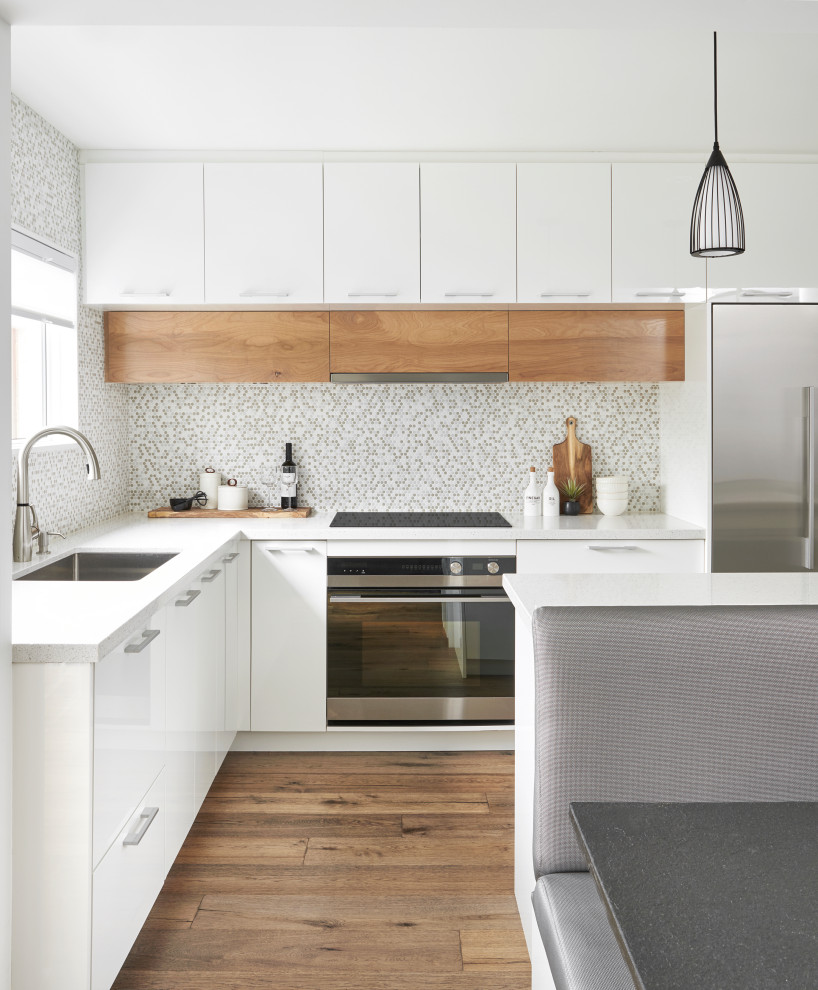 Design ideas for a mid-sized modern l-shaped eat-in kitchen in Toronto with an undermount sink, flat-panel cabinets, white cabinets, quartz benchtops, mosaic tile splashback, stainless steel appliances, medium hardwood floors, with island, white benchtop and multi-coloured splashback.