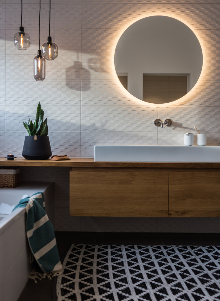 Foto de cuarto de baño único y gris y blanco contemporáneo con suelo gris, armarios con paneles lisos, puertas de armario de madera oscura, bañera empotrada, baldosas y/o azulejos blancos, lavabo sobreencimera y encimeras marrones