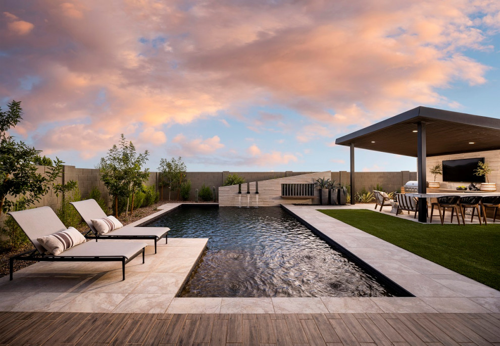 This is an example of a large modern back rectangular infinity swimming pool in Phoenix with a water feature and natural stone paving.