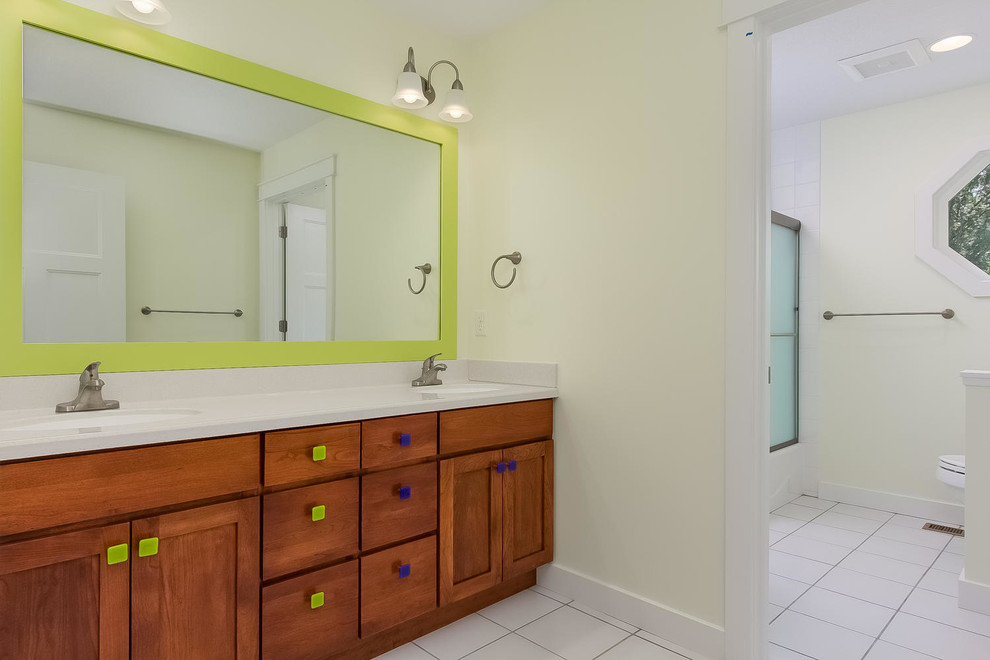 Mid-sized country kids bathroom in Minneapolis with an integrated sink, shaker cabinets, medium wood cabinets, solid surface benchtops, an alcove tub, a shower/bathtub combo, a one-piece toilet, white tile, ceramic tile, green walls and ceramic floors.