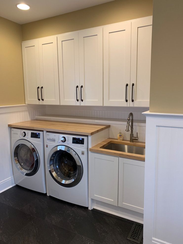 This is an example of a small modern single-wall dedicated laundry room in Baltimore with an undermount sink, shaker cabinets, white cabinets, wood benchtops, beige walls, porcelain floors, a side-by-side washer and dryer, black floor and brown benchtop.