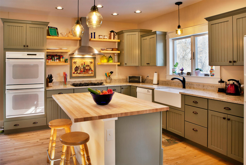 This is an example of a mid-sized arts and crafts l-shaped kitchen in Other with a farmhouse sink, shaker cabinets, green cabinets, medium hardwood floors, with island, brown floor, white appliances and beige benchtop.