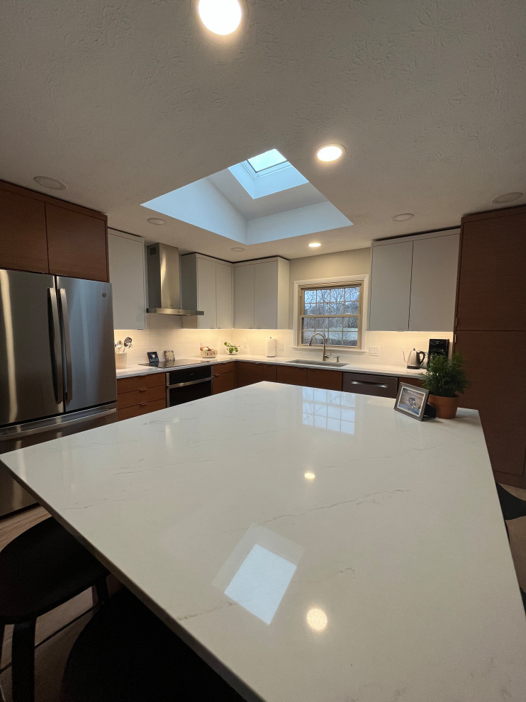 This is an example of a medium sized retro l-shaped kitchen/diner in Indianapolis with a double-bowl sink, flat-panel cabinets, medium wood cabinets, quartz worktops, white splashback, metro tiled splashback, stainless steel appliances, light hardwood flooring, an island, beige floors and white worktops.