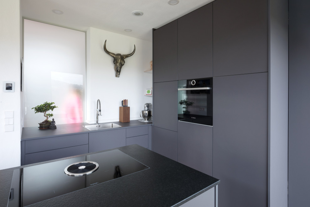 Cette image montre une cuisine ouverte parallèle design de taille moyenne avec des portes de placard grises, un plan de travail en granite, un électroménager noir, parquet foncé, îlot, un sol bleu et un plafond décaissé.