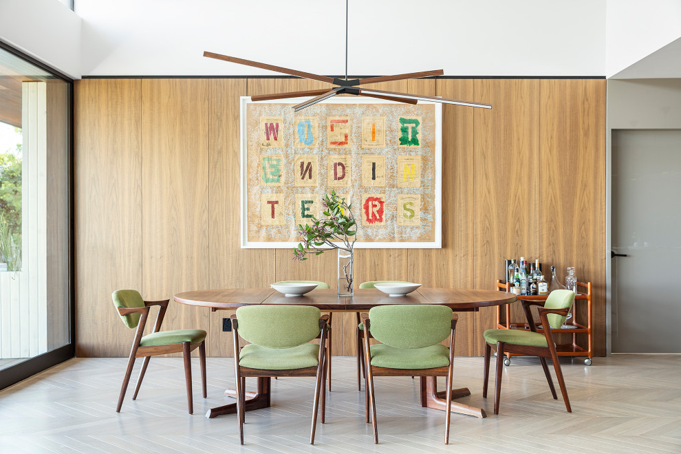 This is an example of a midcentury dining room in Los Angeles with light hardwood floors, no fireplace and wood walls.
