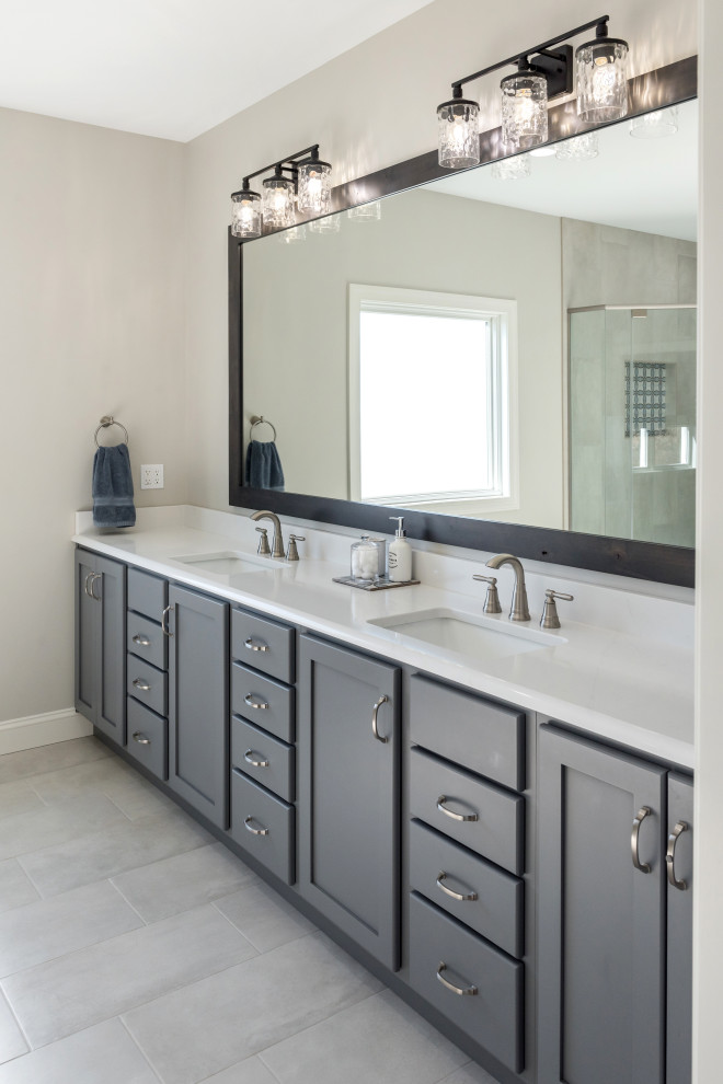 Photo of a large transitional master bathroom in St Louis with shaker cabinets, grey cabinets, white tile, stone slab, grey walls, vinyl floors, an undermount sink, engineered quartz benchtops, grey floor, a hinged shower door, white benchtops, a shower seat, a double vanity and a freestanding vanity.