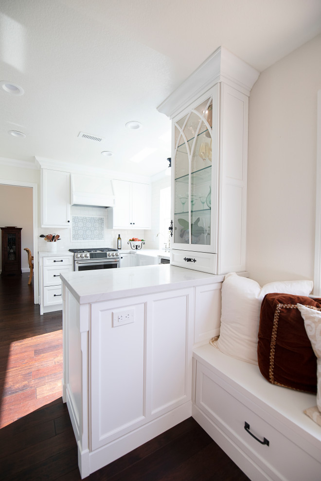 Inredning av ett klassiskt avskilt, litet vit vitt u-kök, med en rustik diskho, luckor med infälld panel, vita skåp, bänkskiva i kvarts, vitt stänkskydd, mellanmörkt trägolv och en halv köksö
