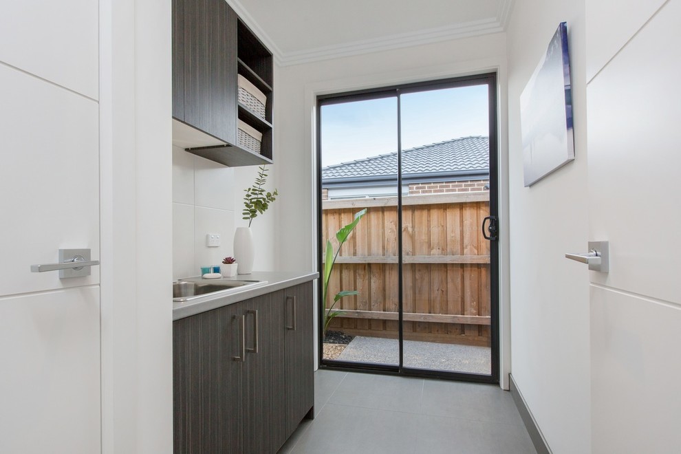 Mid-sized modern galley dedicated laundry room in Melbourne with a single-bowl sink, laminate benchtops, white walls, porcelain floors and a stacked washer and dryer.