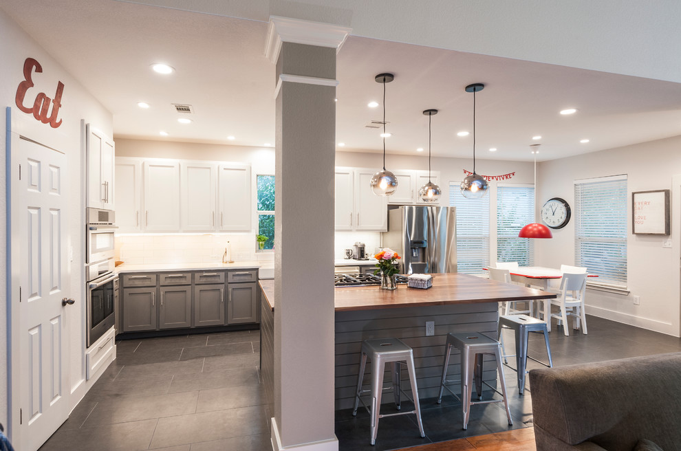Photo of a large transitional l-shaped open plan kitchen in Austin with a farmhouse sink, shaker cabinets, white cabinets, quartz benchtops, white splashback, ceramic splashback, stainless steel appliances, ceramic floors and with island.