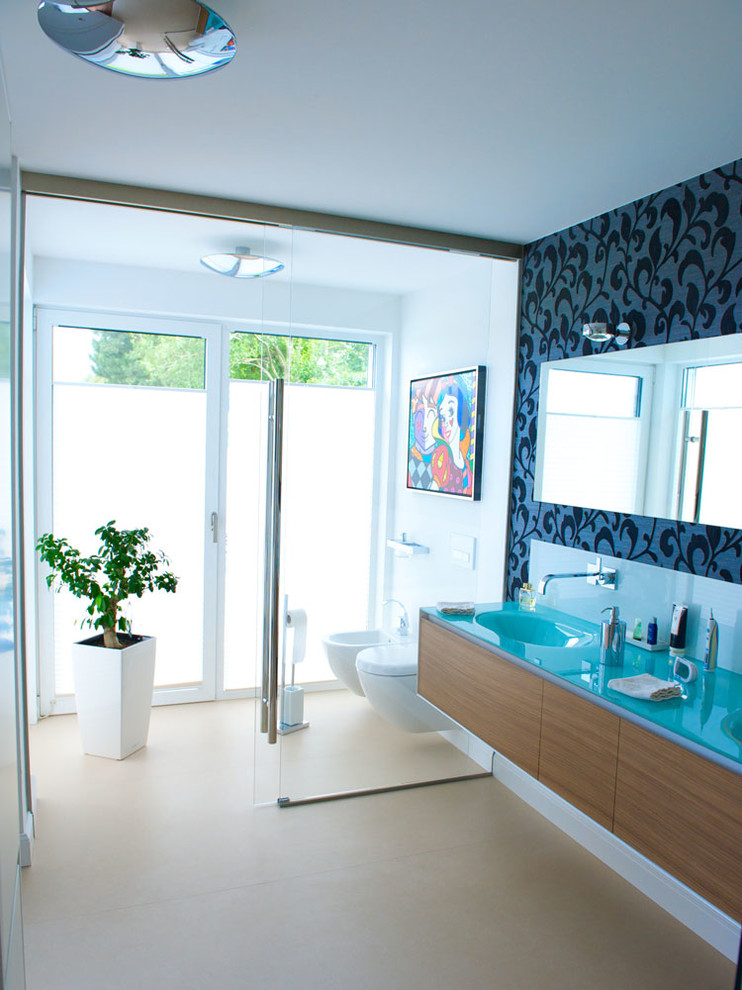 Badezimmer En Suite With hellbraunen Holzschränken, Wandtoilette, beigen Fliesen, Steinfliesen, blauer Wandfarbe, integriertem Waschbecken and Glaswaschbecken/Glaswaschtisch in Dusseldorf